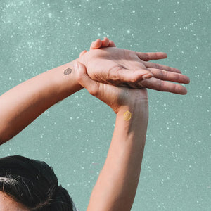 woman reaching arms over head with temporary tattoos on wrists representing kindness.