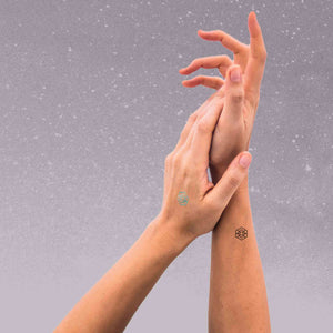 A woman wearing mindful marks is lightly touching her palm to the wrist of her other hand.