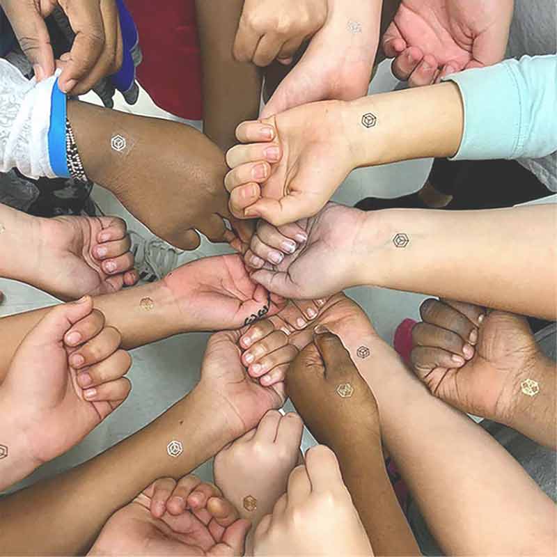 A diverse group of about a dozen people wearing mindful marks on their wrists and hands, fist bumping in a circle pattern.