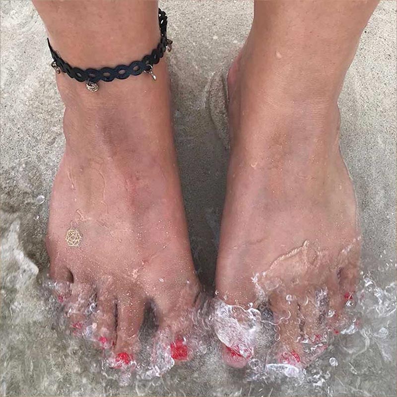 woman's feet standing at ocean's edge wearing mindful mark representing transformation