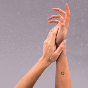 A woman wearing mindful marks is lightly touching her palm to the wrist of her other hand.