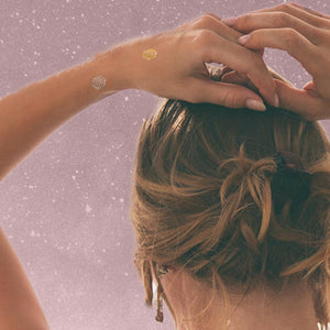 woman facing away from camera with hands above head wearing mindfulness tattoos on wrist and hand