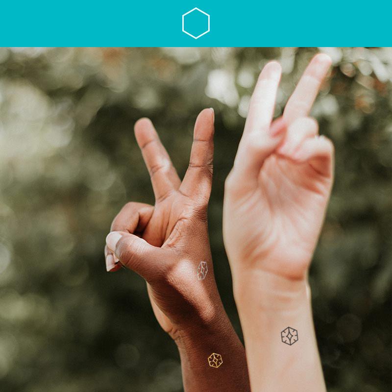 Two women both holding two fingers up making a peace sign and wearing Mindful Marks on their wrists representing peace.